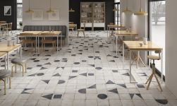 Restauracja z drewnianymi stołami, krzesłami, taboretami, szarą kanapą, lampami wiszącymi, szafą z oszklonymi drzwiami i płytkami z kolekcji Maison