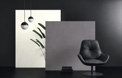 Kompozycja artystyczna ze ścianką pokrytą szarymi płytkami z kolekcji Lins, skórzanym czarnym fotelem, i lampą wiszącą