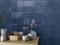 Granatowa ściana w kuchni wyłożona płytkami z kolekcji Lins z drewnianym stołem i naczyniami