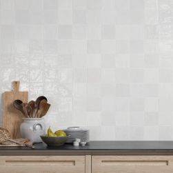 Biała ściana w kuchni wyłożona cegiełkami z kolekcji Riad z drewnianymi meblami i ciemnym blatem oraz naczyniami