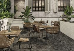 Restauracja z kwadratowymi stolikami, wiklinowymi krzesłami, kwiatami i płytkami z kolekcji FS Etna