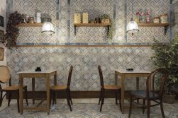 Restauracja z dwoma stolikami, czterema krzesłami, wiszącymi p&oacute;łkami na ścianie, kwiatami i płytkami z kolekcji FS Roots