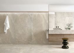 Minimalistyczna łazienka wyłożona beżowymi płytkami imitującymi kamień Lucca Beige z wiszącą szafką z kamiennym blatem, stołkiem, dużym lustrem i białym ręcznikiem na ścianie