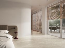 Przestronna, minimalistyczna sypialnia wyłożona beżowymi płytkami imitującymi kamień Lucca Beige, z łóżkiem z brązowym zagłówkiem, oknami i drzwiami na całej ścianie prowadzącymi na taras