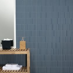 Ściana łazienki wyłożona płytkami Beat Blue z drewnianą półką, białym ręcznikiem i dozownikiem na mydło