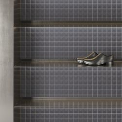 Metalowe półki na tle ściany wyłożonej płytkami z kolekcji Pique oraz z parą męskich butów wyjściowych