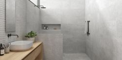Łazienka wyłożona szarymi płytkami imitującymi kamień Lucca Grey z prysznicem oddzielonym ścianką, drewnianą szafką z białą umywalką nablatową oraz podłużnym lustrem