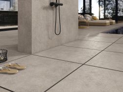 Basen z podłogą wyłożoną płytkami imitującymi beton Asphalt Mud z prysznicem oraz dwoma leżakami i stolikiem