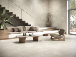 Salon wyłożony jasnymi płytkami imitującymi beton Asphalt Off White ze schodami, kanapą, fotelem i stolikiem