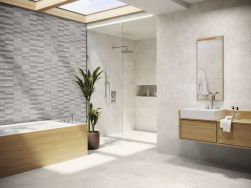 Łazienka wyłożona jasnymi płytkami imitującymi beton Asphalt Off White z zabudowaną wanną, kabiną prysznicową i drewnianą szafką wiszącą z umywalką oraz lustrem