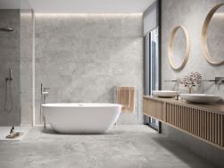 Łazienka wyłożona szarymi płytkami imitującymi kamień Dome Ash z kabiną prysznicową, wanną wolnostojącą i wiszącą p&oacute;łką z dwiema umywalkami nablatowymi i dwoma okrągłymi lustrami