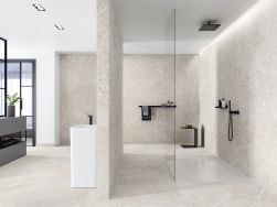 Łazienka wyłożona płytkami imitującymi kamień lastryko Volcano Bianco z dużą kabiną prysznicową, półkami na ścianie i białą umywalką stojącą