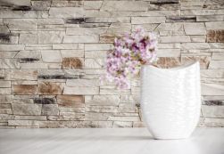 Ściana wyłożona kamieniem dekoracyjnym Castor Frio z białym wazonem z różowym kwiatkiem na jasnym blacie