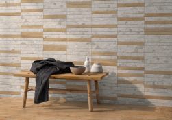 Ściana wyłożona biało-brązowymi płytkami imitującymi kamień i drewno oraz ława z ręcznikiem i naczyniami