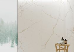 Widok na ścianę wyłożoną wielkoformatowymi płytkami imitującymi marmur białymi ze złotymi żyłami Dual White SP z małym taboretem z kosmetykami do kąpieli i małymi ręcznikami