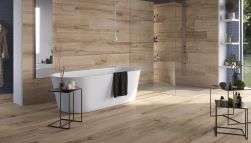 Łazienka wyłożona płytkami drewnopodobnymi z kolekcji Millelegni Remake Rovere Ossidato, z białą wanną wolnostojącą, kabiną prysznicową, małymi stolikami i wąskim lustrem