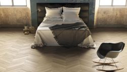 Przytulna, rustykalna sypialnia z drewnopodobną podłogą w jodełkę z kolekcji Sleekwood z podwójnym łóżkiem, bujanym krzesłem i lampką