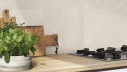 Zbliżenie na ścianę w kuchni wyłożoną beżowymi płytkami imitującymi kamień z kolekcji Nordika z drewnianym blatem z kuchenką, deską i kwiatem