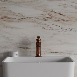 Widok od przodu na białą umywalkę z baterią stojącą w kolorze miedzi antycznej Omnires Armance na tle jasnej, kolorowej, marmurowej ściany
