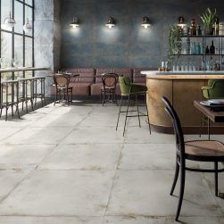 Restauracja, stoliki, krzesła, ściany wyłożone niebieskimi płytkami, na podłodze Flamed Ice Natural Rect. 59,55x59,55 płytki imitujące metal