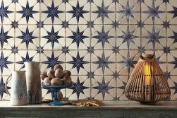 Ściana wyłożona patchworkowymi płytkami we wzór w niebieskie gwiazdy FS Star Blue LT z drewnianą ławą z lampionem, dwoma wazonami i misą z orzechami