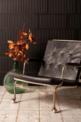Pokój z jasną podłogą i czarną ścianą wyłożoną płytkami z reliefową powierzchnią FS Loft Black, z krzesłem i wazonem z jesiennymi liśćmi