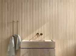 Ściana w łazience wyłożona jasnymi płytkami drewnopodobnymi ze żłobieniami Granier Natural, ze ścienną umywalką z szafką i ręcznikiem na wieszaku