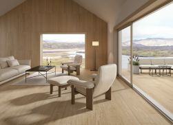 Przytulny salon z podłogą wyłożoną płytkami drewnopodobnymi Granier Taupe, z kanapą, dwoma fotelami, czarnym stolikiem na dywanie, wyjściem na taras i widokiem na góry
