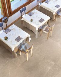 Restauracja z podłogą wyłożoną beżowymi płytkami imitującymi kamień Groove Nude Beige, z kwadratowymi stołami z obrusami i zastawą oraz z krzesłami