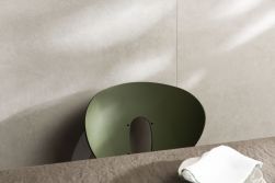 Ściana wyłożona jasnymi płytkami imitującymi beton Ground Bone z zielonym krzesłem przy stole