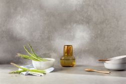 Szara płytka imitująca beton Ground Grey na ścianie i na podłodze, ze szklanym wazonem, miskami, drewnianymi łyżkami i szparagami
