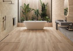 Przytulna łazienka wyłożona płytkami drewnopodobnymi brązowymi Grow Kalua SP z roślinami na jednej ścianie, białą wanną wolnostojącą, szarą betonową umywalką i półką wiszącą, lustrem oraz ścianką prysznicową