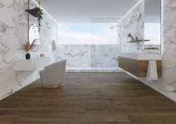 Elegancka łazienka z ciemną drewnopodobną podłogą wyłożoną płytkami Grow Porto SP i marmurowymi ścianami, z dużą kabiną prysznicową, z wiszącą półką drewnianą z umywalką i prostokątnym lustrem oraz białą półką toaletką z okrągłym lustrem i fotelem
