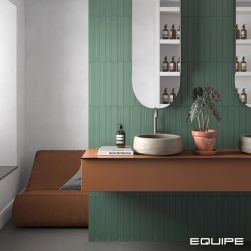 Ściana w łazience wyłożona zielonymi płytkami Hopp Bro Green z brązową półką, dwiema umywalkami nablatowymi i dwoma lustrami