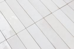 Zbliżenie na powierzchnię odbijającą światło białych, rustykalnych cegiełek ściennych Tribeca Gypsum White 6x24,6