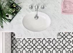 Widok z góry na podłogę w łazience wyłożoną biało-czarną mozaiką Manorial Carrara White Manor z szafką z marmurowym blatem, umywalką, różowym ręcznikiem i kwiatem