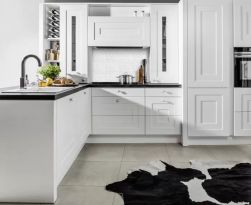 Jasna kuchnia z fragmentem ściany wyłożonym białą mozaiką Manorial Carrara White Armor z białymi meblami z czarnymi blatami i biało-czarnym dywanem