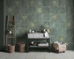 Przy ścianie na półce szara umywalka, niżej ręczniki kąpielowe, przy półce dekoracyjna drabina z powieszoną rośliną, na podłodze dwa kosze wiklinowe, podłoga wyłożona białymi płytkami ze złotą żyłą, na ścianie na przemian ułożone zielone płytki z wytłoczo