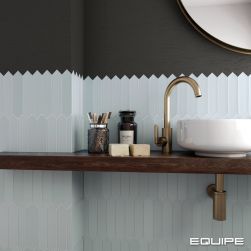 Widok na ścianę w nowoczesnej łazience do połowy wyłożonej błękitnymi cegiełkami z kolekcji Lanse, a do połowy pomalowanej czarną farbą, z drewnianą półką wisząca, białą umywalką nablatową z baterią stojącą i kosmetykami oraz okrągłym lustrem