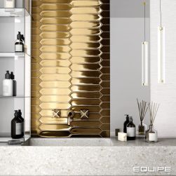 Widok na ścianę w łazience wyłożoną w części złotymi cegiełkami z kolekcji Lanse, z półką lastryko z umywalką wpuszczaną w blat i baterią podtynkową oraz szklaną szafką z półkami i kosmetykami