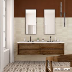 Rustykalna łazienka ze ścianą w części wyłożoną beżowymi cegiełkami z kolekcji Lanse i pomalowaną brązową farbą, z drewnianą półką wiszącą z dwiema umywalkami i dwoma prostokątnymi lustrami, lampą wiszącą, krzesłem, oknem z białymi zasłonami oraz patchwor