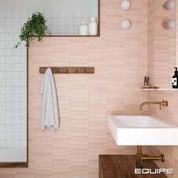 Fragment łazienki ze ścianą wyłożoną różowymi cegiełkami z kolekcji Lanse oraz białymi kafelkami, z drewnianą szafką, bialą umywalką z baterią podtynkową, dwoma kulistymi kinkietami, wieszakiem z ręcznikiem i kwiatem