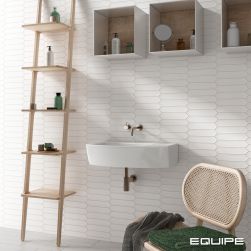 Fragment jasnej łazienki ze ścianą wyłożoną białymi cegiełkami z kolekcji Lanse z wiszącą  umywalką białą, krzesłem z ręcznikami, trzema wiszącymi półkami z kosmetykami i drabiną z półeczkami