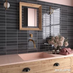 Fragment łazienki z różowo-czarną ścianą wyłożoną czarnymi cegiełkami z kolekcji Limit z drewnianą szafką z umywalką i baterią podtynkową, lustrem w drewnianej ramie, dwoma kinkietami i kwiatami