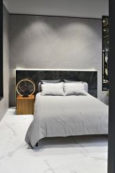 Sypialnia ze ścianą wyłożoną jasnoszarymi płytkami imitującymi kamień Mainstone Dolphin NT z łóżkiem, ciemnym zagłówkiem i stolikiem z lampą