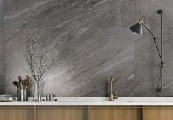 Widok na ścianę w kuchni wyłożoną ciemnoszarymi płytkami imitującymi kamień Mainstone Moon NT z drewnianymi meblami z białym blatem i dużą lampą kinkietem