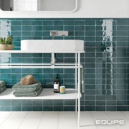 Fragment łazienki ze ścianą do połowy wyłożoną turkusowymi cegiełkami z kolekcji Manacor, białym stolikiem z umywalką nablatową, ręcznikiem i kosmetykami oraz lustrem