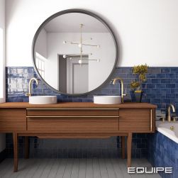 Łazienka ze ścianą wyłożoną do połowy niebieskimi cegiełkami z kolekcji Manacor z ciemną, drewnianą szafką, dwoma umywalkami nablatowymi, dużym okrągłym lustrem i wanną zabudowaną płytkami