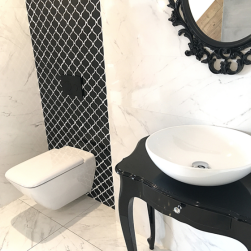 Elegancka łazienka z fragmentem ściany za miską WC wyłożoną czarną mozaiką Mini Arabesco Black, z czarnym stolikiem z umywalką nablatową i lustrem w ramie