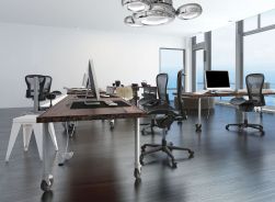 Białe biuro z drewnianymi biurkami, czarnymi krzesłami i srebrną lampą sufitową